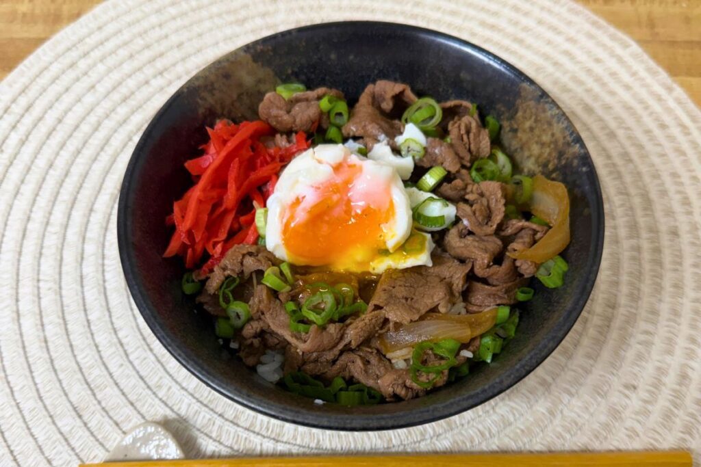 Gyudon beef bowl topped with soft-cooked egg, green onion, and pickled ginger