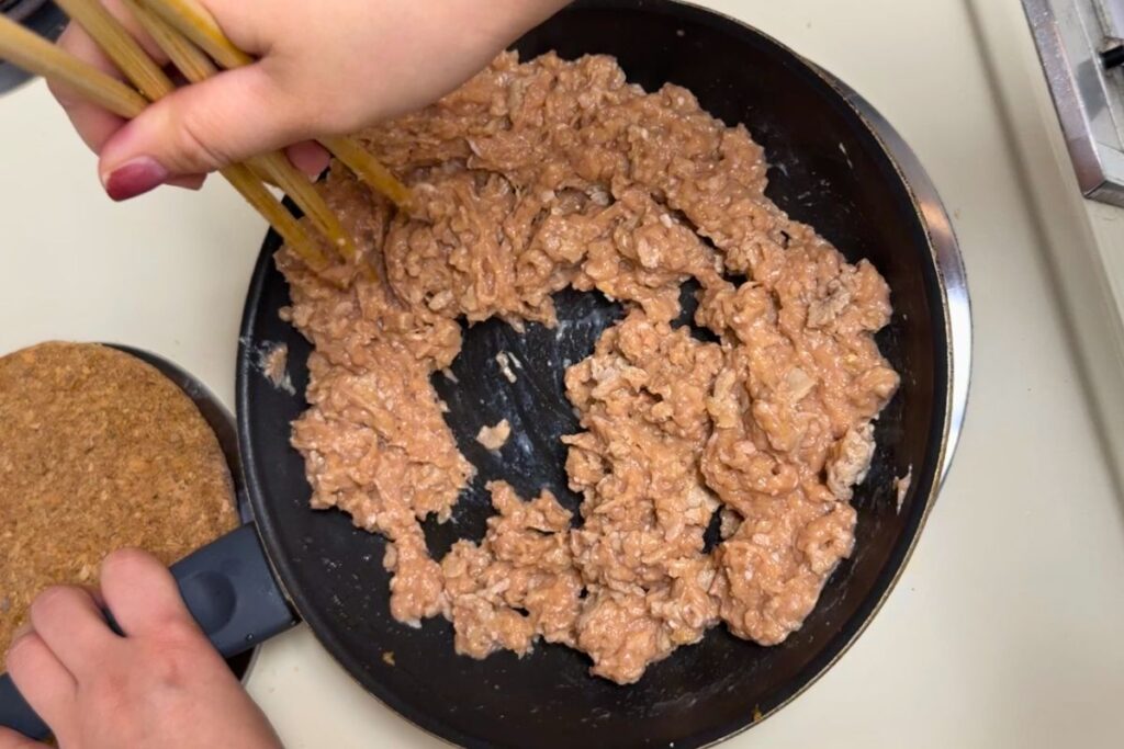 Cooking ground chicken soboro in a pan while breaking it apart with chopsticks